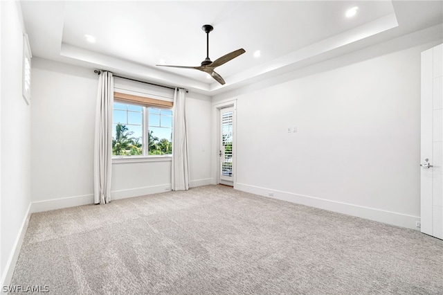 empty room featuring a tray ceiling, ceiling fan, and light carpet