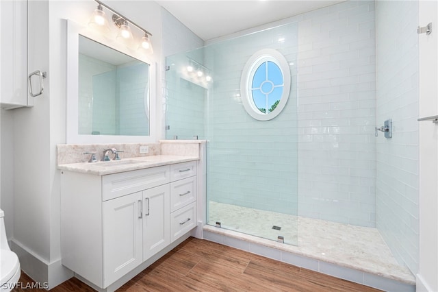 bathroom with a tile shower, vanity, hardwood / wood-style flooring, and toilet