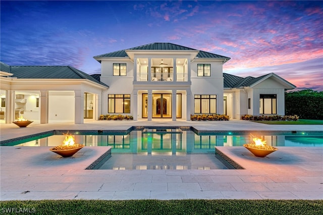 back house at dusk featuring ceiling fan, a fire pit, a balcony, a fenced in pool, and a patio