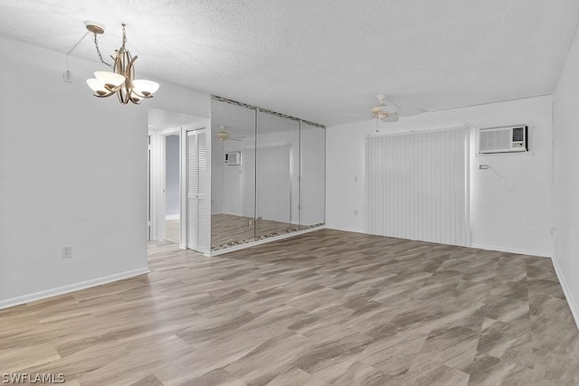 empty room with ceiling fan with notable chandelier, a textured ceiling, a wall unit AC, and light hardwood / wood-style flooring