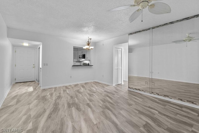 unfurnished living room featuring ceiling fan with notable chandelier, light wood-type flooring, and a textured ceiling