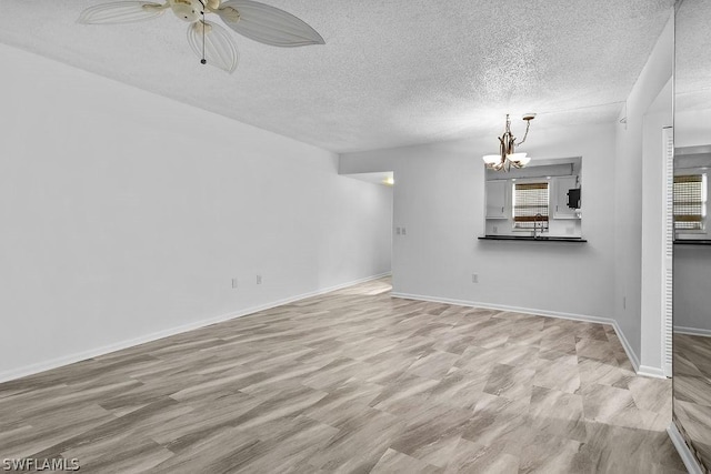 unfurnished living room with ceiling fan with notable chandelier and a textured ceiling