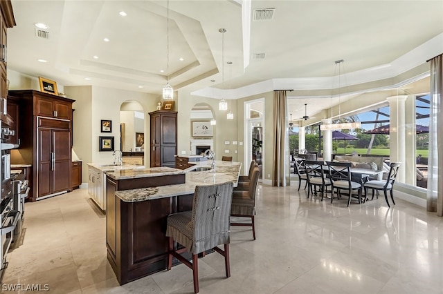 kitchen featuring sink, a breakfast bar, decorative light fixtures, a raised ceiling, and a large island with sink