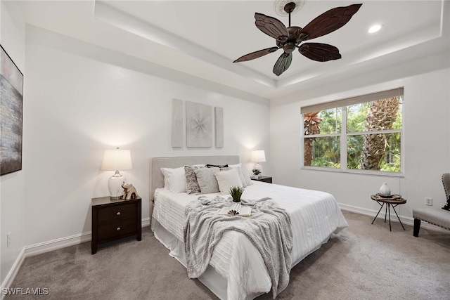 carpeted bedroom featuring a tray ceiling and ceiling fan