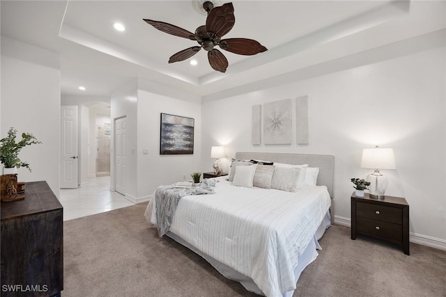 carpeted bedroom featuring a tray ceiling, connected bathroom, and ceiling fan