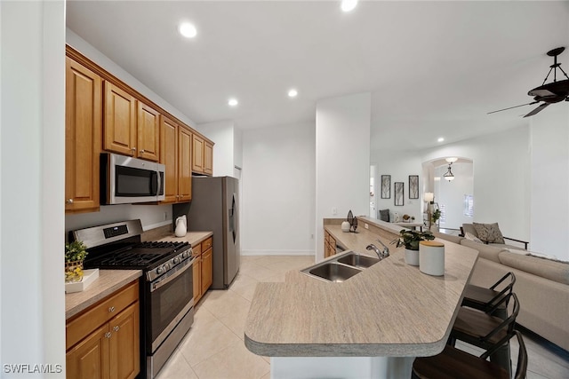 kitchen with appliances with stainless steel finishes, a breakfast bar, light tile patterned floors, sink, and ceiling fan