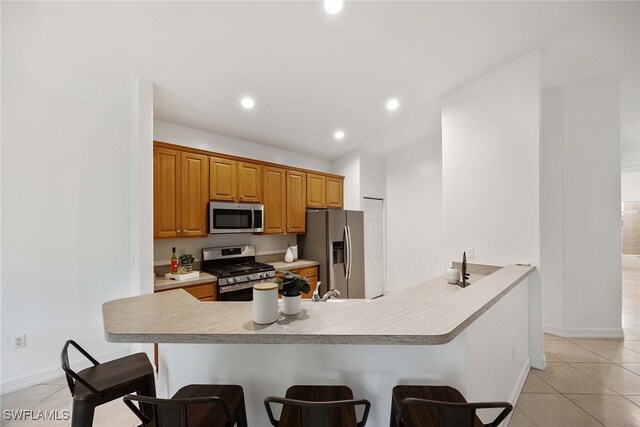 kitchen featuring a kitchen breakfast bar, light tile patterned floors, stainless steel appliances, and kitchen peninsula