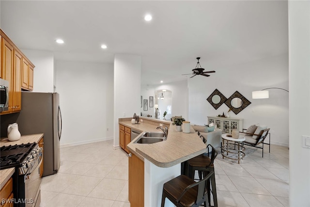 kitchen with a kitchen bar, sink, light tile patterned flooring, stainless steel appliances, and kitchen peninsula