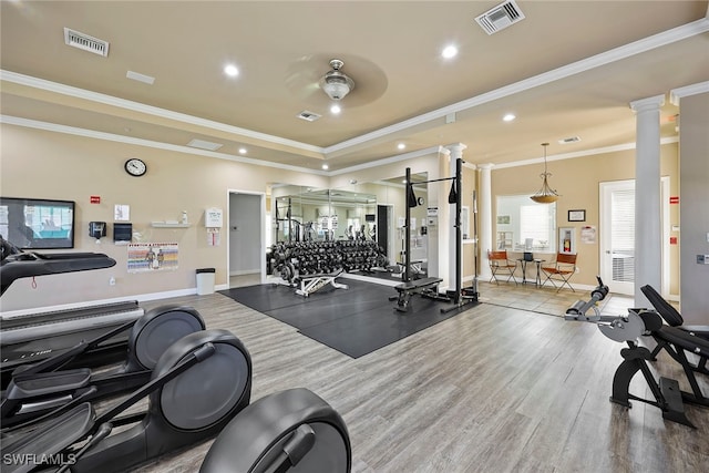 workout area featuring ceiling fan, crown molding, hardwood / wood-style floors, a tray ceiling, and ornate columns