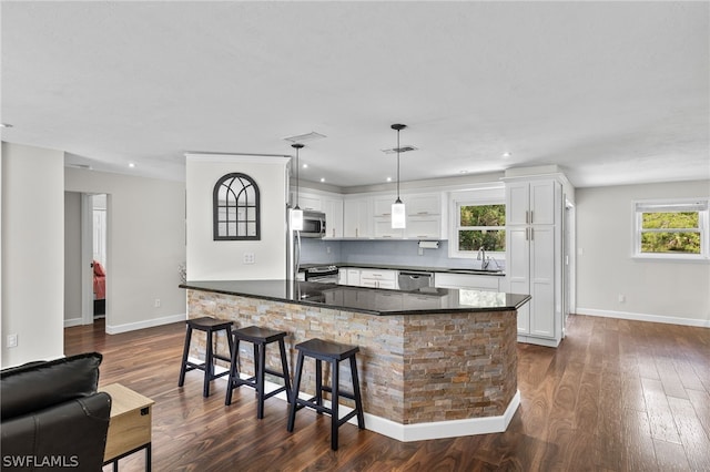 kitchen with decorative light fixtures, white cabinets, a kitchen island, appliances with stainless steel finishes, and dark wood-type flooring