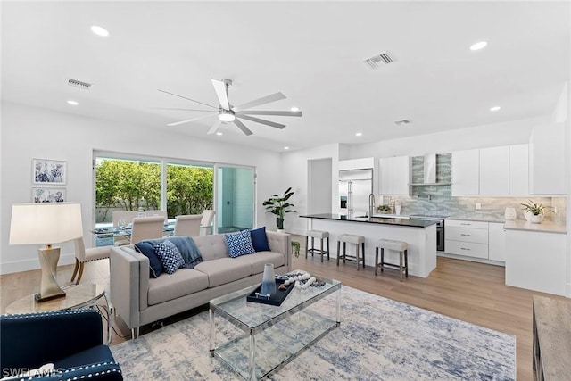 living room featuring light hardwood / wood-style flooring, ceiling fan, and sink