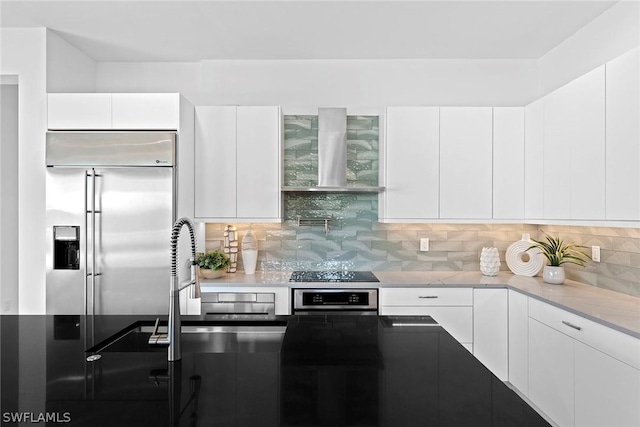 kitchen with white cabinetry, wall chimney exhaust hood, wall oven, stainless steel built in refrigerator, and backsplash