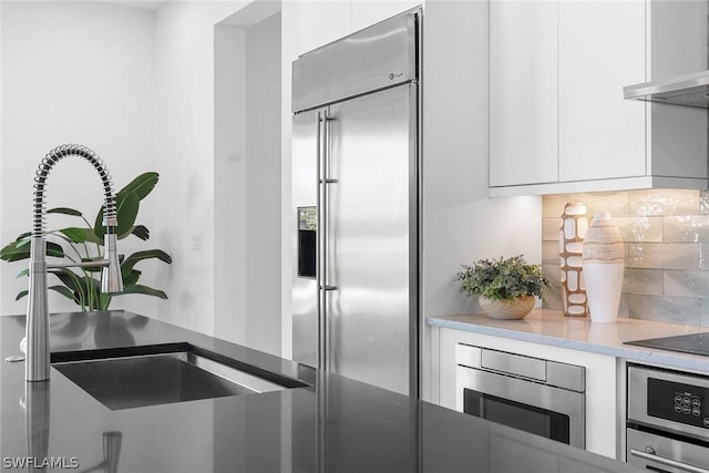 kitchen featuring backsplash, white cabinets, wall chimney range hood, sink, and stainless steel appliances