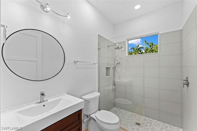 bathroom featuring a tile shower, vanity, and toilet