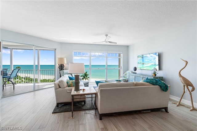 living room featuring hardwood / wood-style flooring, a textured ceiling, a water view, and ceiling fan