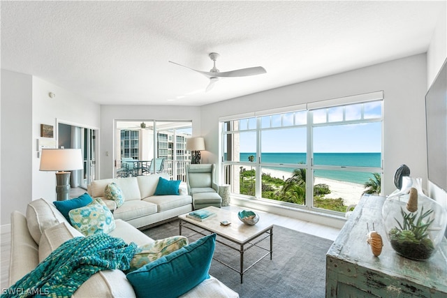 living room featuring a water view, a textured ceiling, ceiling fan, and a healthy amount of sunlight