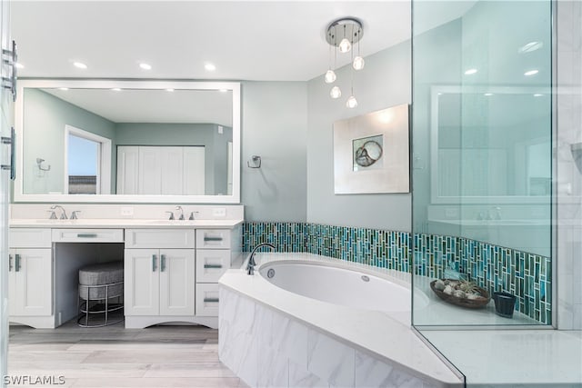 bathroom with dual vanity and tiled tub