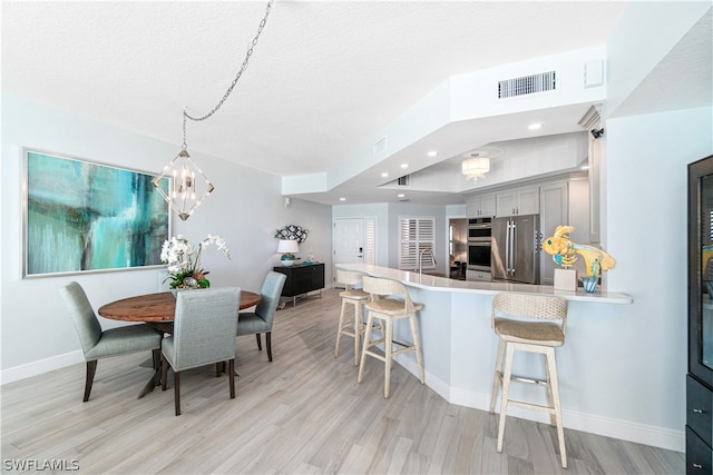 kitchen featuring kitchen peninsula, stainless steel appliances, light hardwood / wood-style floors, a kitchen bar, and gray cabinetry