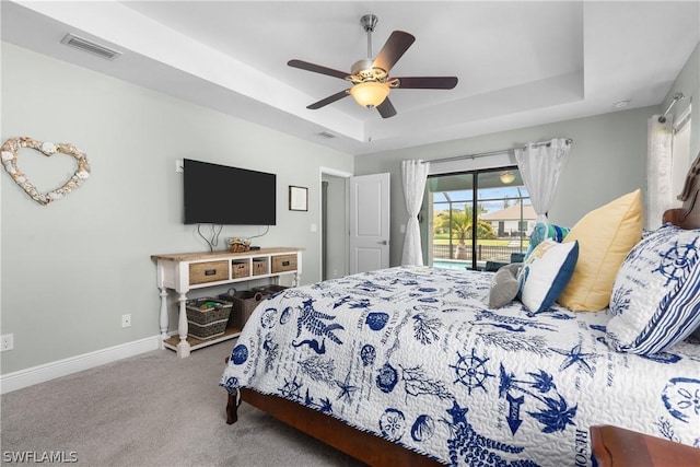 carpeted bedroom featuring access to exterior, a tray ceiling, and ceiling fan