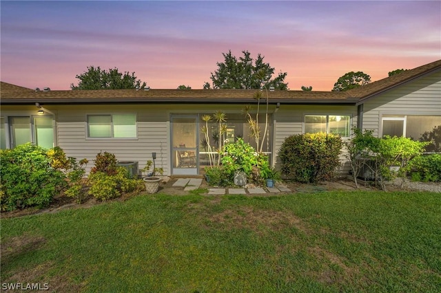 back house at dusk featuring a lawn and central air condition unit