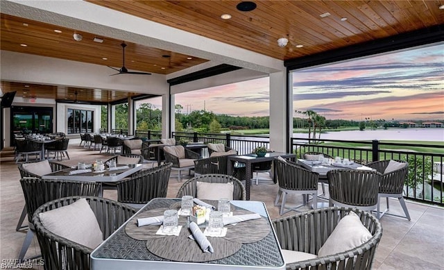 patio terrace at dusk with a water view, ceiling fan, and an outdoor hangout area