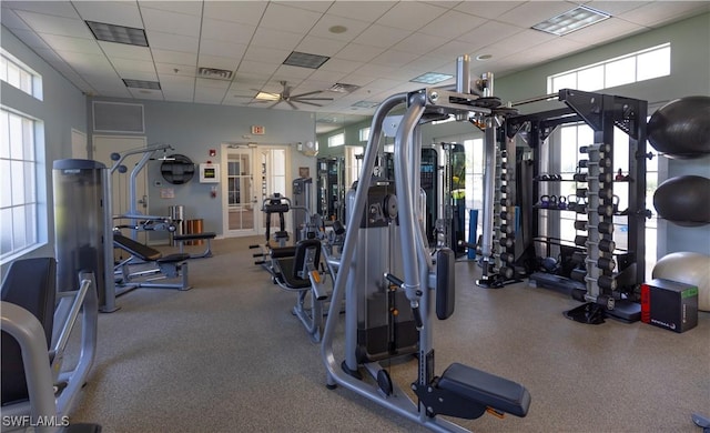 exercise room featuring a paneled ceiling, ceiling fan, and plenty of natural light