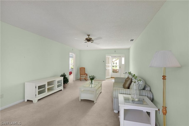 living room with a textured ceiling, light colored carpet, and ceiling fan