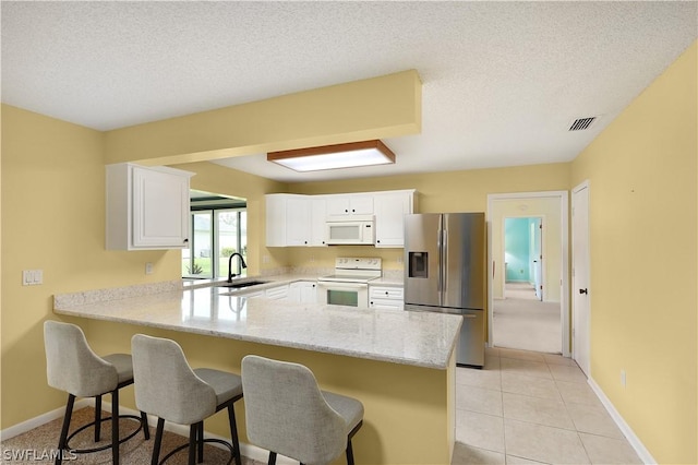 kitchen with white cabinets, a kitchen breakfast bar, white appliances, and kitchen peninsula