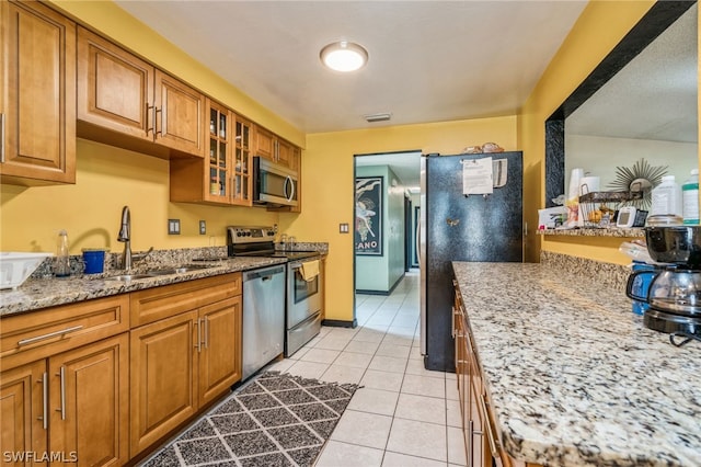 kitchen with sink, light stone countertops, stainless steel appliances, and light tile patterned floors