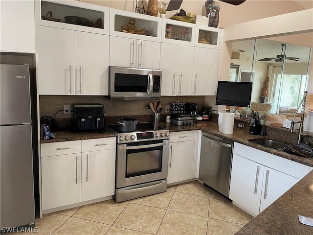 kitchen with stainless steel appliances, white cabinets, light tile patterned flooring, decorative backsplash, and dark stone counters