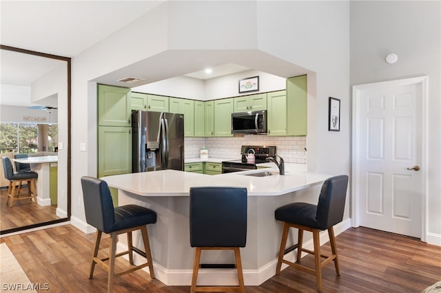 kitchen featuring tasteful backsplash, green cabinetry, a kitchen bar, kitchen peninsula, and stainless steel appliances