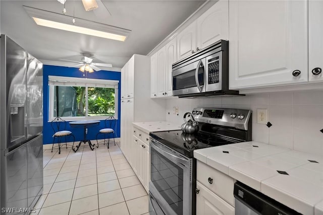 kitchen featuring tile countertops, light tile patterned floors, white cabinetry, appliances with stainless steel finishes, and ceiling fan