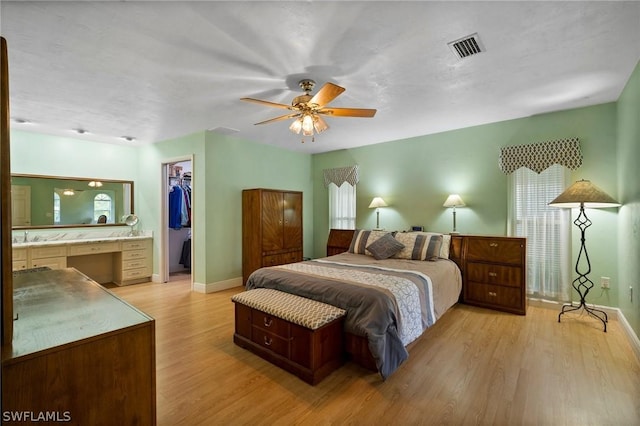 bedroom with a closet, built in desk, light wood-type flooring, ceiling fan, and a spacious closet