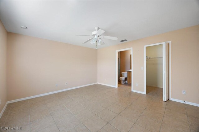 unfurnished bedroom with a closet, a walk in closet, ensuite bathroom, light tile patterned floors, and ceiling fan