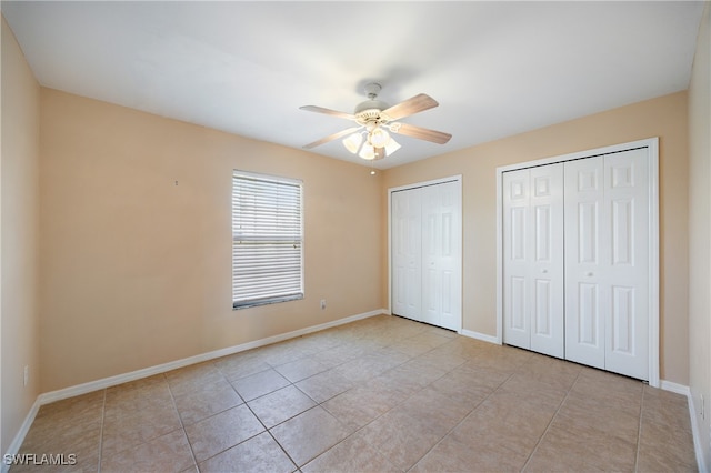 unfurnished bedroom featuring ceiling fan, two closets, and light tile patterned floors