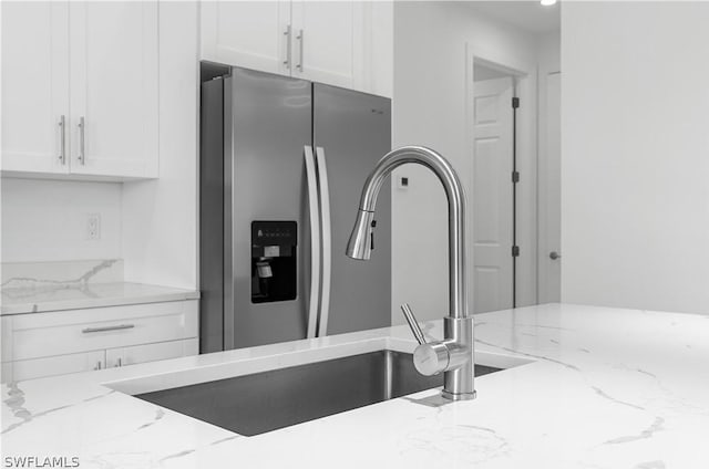 interior details featuring stainless steel fridge, light stone countertops, sink, and white cabinets