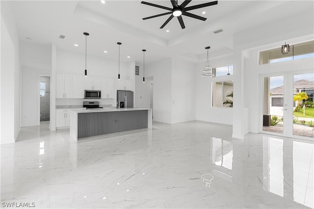 kitchen featuring pendant lighting, ceiling fan, an island with sink, appliances with stainless steel finishes, and white cabinetry