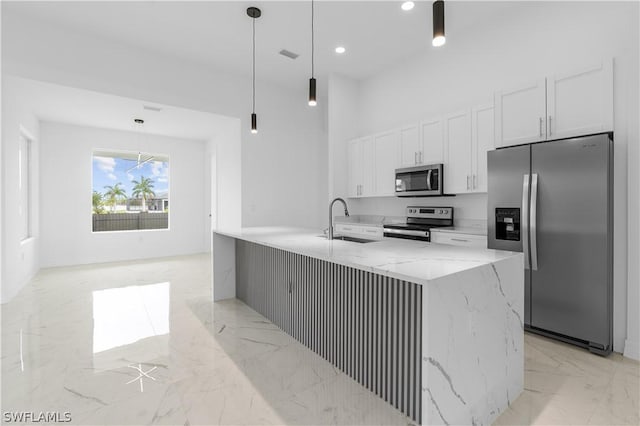 kitchen with appliances with stainless steel finishes, light stone counters, sink, white cabinets, and hanging light fixtures