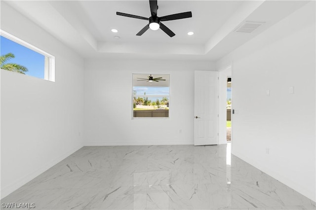 empty room featuring plenty of natural light, ceiling fan, and a tray ceiling