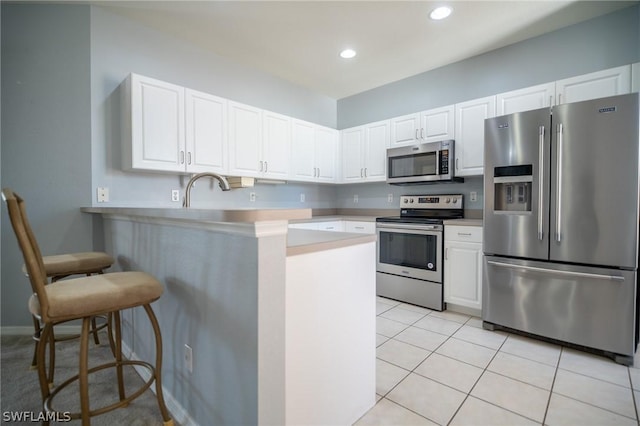 kitchen with white cabinetry, kitchen peninsula, a breakfast bar, light tile patterned flooring, and appliances with stainless steel finishes