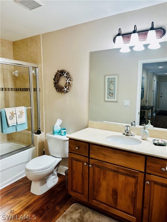 full bathroom with vanity, hardwood / wood-style flooring, enclosed tub / shower combo, and toilet