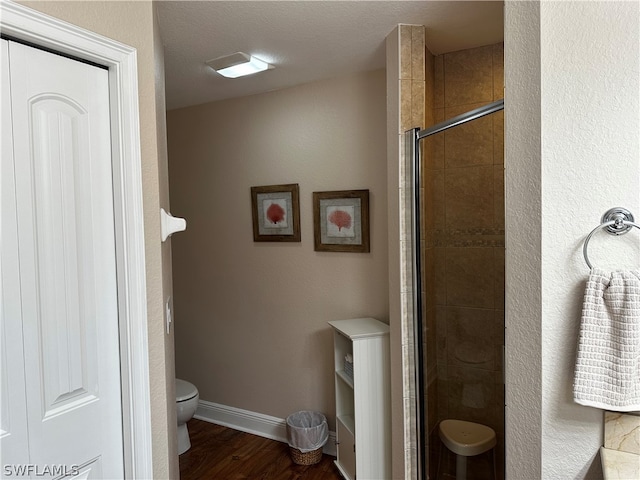 bathroom with toilet, a shower with door, a textured ceiling, and hardwood / wood-style floors