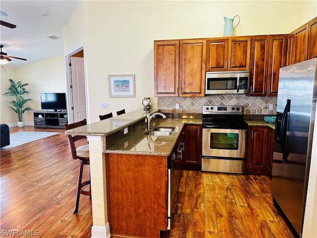 kitchen with stainless steel appliances, sink, kitchen peninsula, dark wood-type flooring, and ceiling fan