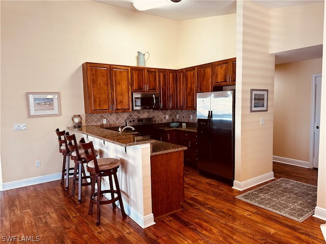 kitchen featuring kitchen peninsula, dark stone counters, backsplash, dark hardwood / wood-style flooring, and appliances with stainless steel finishes