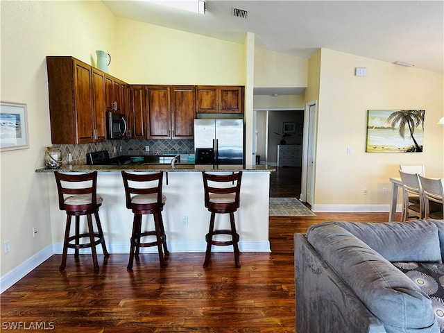 kitchen with a kitchen bar, decorative backsplash, dark hardwood / wood-style floors, and stainless steel appliances