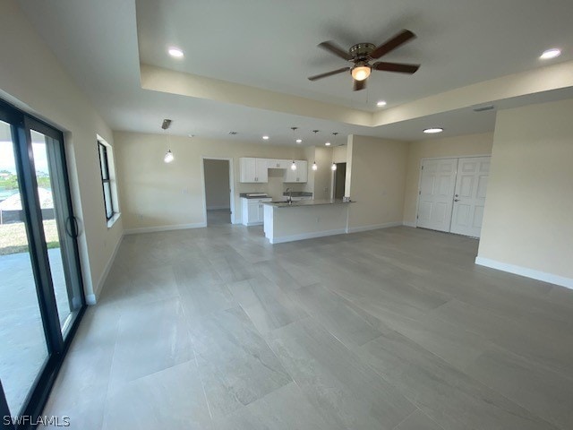 unfurnished living room featuring ceiling fan and a tray ceiling