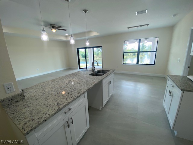 kitchen featuring a kitchen island with sink, hanging light fixtures, sink, and white cabinets