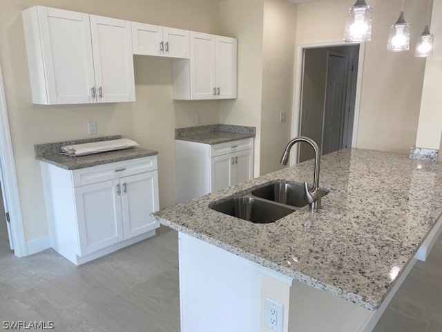 kitchen featuring white cabinetry, sink, light stone counters, and hanging light fixtures