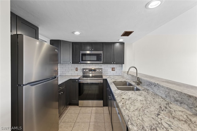 kitchen with sink, stainless steel appliances, light stone counters, and decorative backsplash