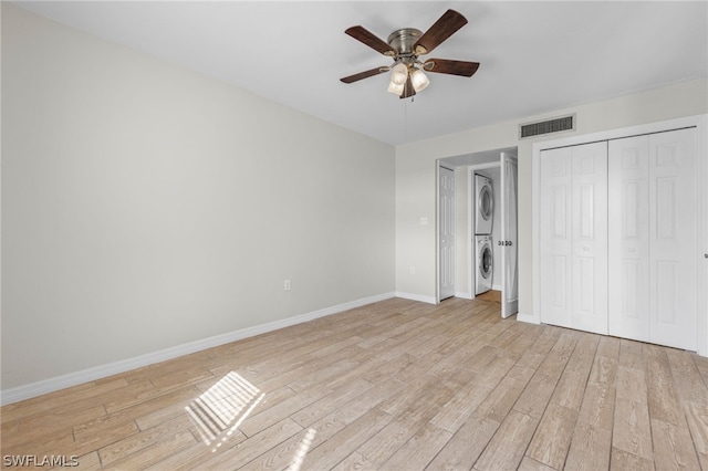 unfurnished bedroom featuring ceiling fan, light wood-type flooring, a closet, and stacked washer and dryer